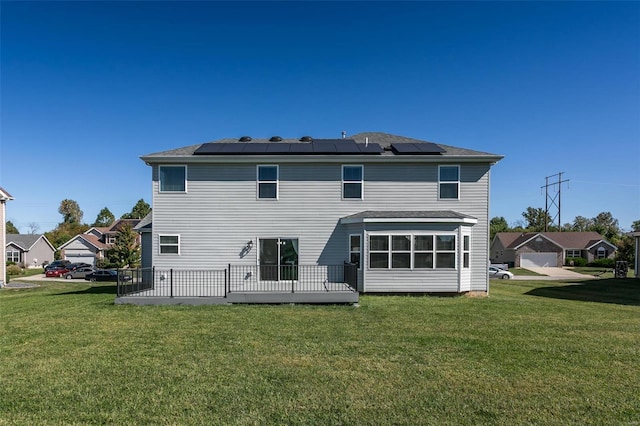 rear view of house with a wooden deck, a lawn, and solar panels