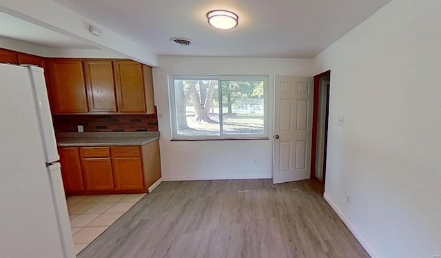 kitchen with white refrigerator, light wood-type flooring, and tasteful backsplash