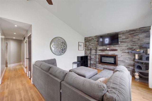 living room with lofted ceiling, a stone fireplace, and light hardwood / wood-style floors