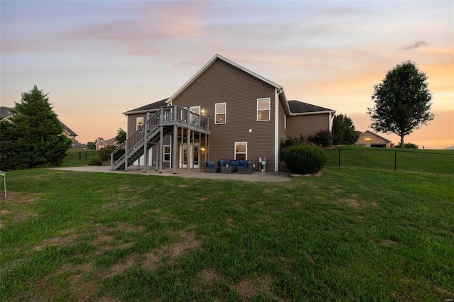 back house at dusk with a wooden deck, a lawn, and a patio area