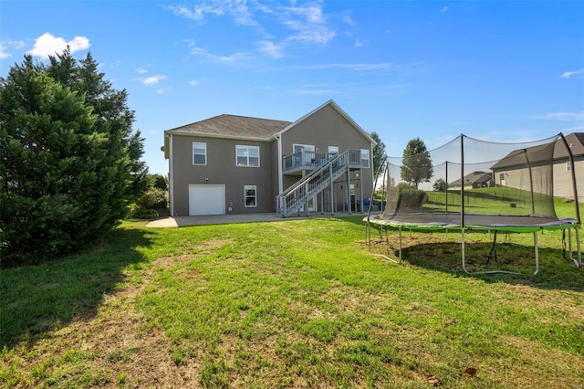 rear view of property with an attached garage, a yard, driveway, stairway, and a trampoline