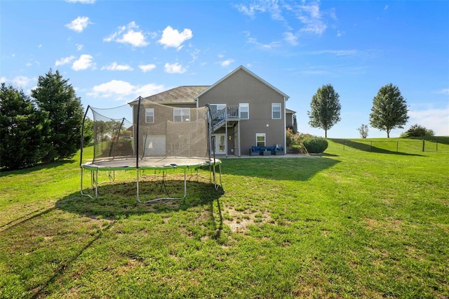 rear view of house with a lawn, a trampoline, fence, and a balcony