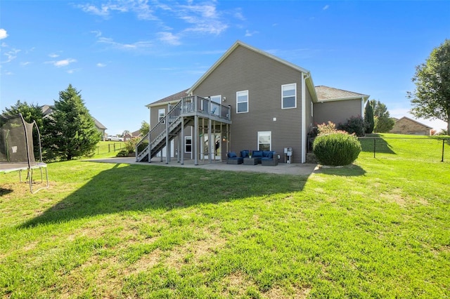 back of property with a trampoline, a deck, a lawn, and a patio area