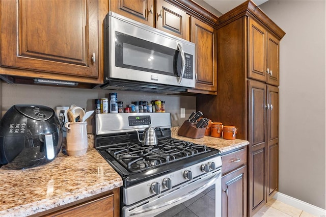 kitchen featuring light tile patterned floors, light stone countertops, and stainless steel appliances