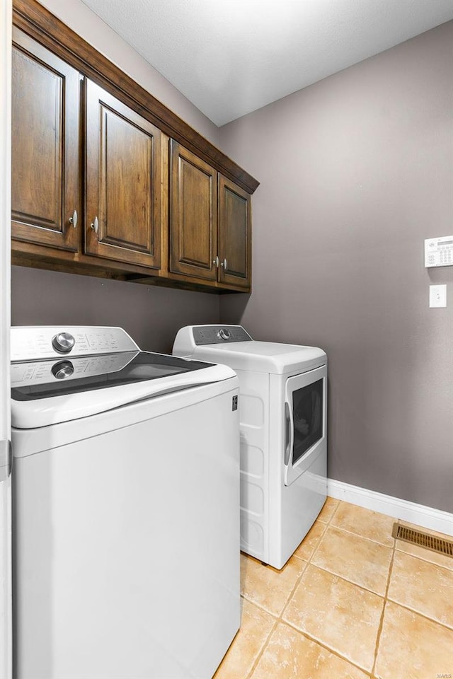 clothes washing area featuring washer and dryer, light tile patterned floors, and cabinets