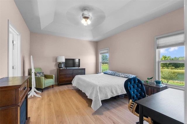 bedroom featuring a raised ceiling, light wood-type flooring, and ceiling fan