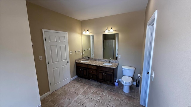 bathroom with double vanity, toilet, a sink, tile patterned flooring, and baseboards