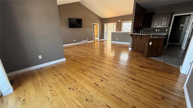 kitchen with open floor plan, dark brown cabinets, light wood-style flooring, and visible vents