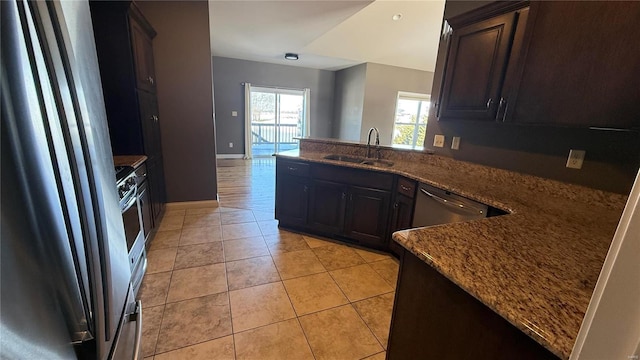 kitchen with light tile patterned floors, stainless steel appliances, a sink, dark stone counters, and a peninsula