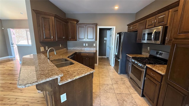 kitchen featuring light stone counters, dark brown cabinetry, stainless steel appliances, a peninsula, and a sink