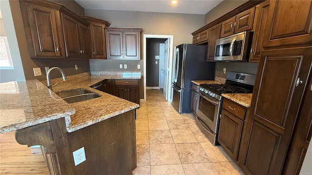 kitchen featuring light stone counters, light tile patterned floors, stainless steel appliances, a sink, and a peninsula