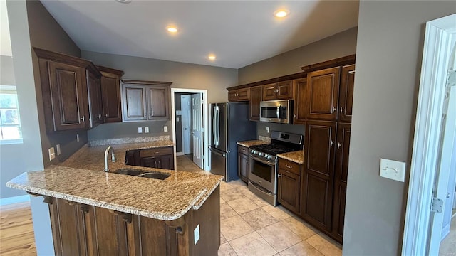 kitchen with a peninsula, dark brown cabinetry, stainless steel appliances, and a sink