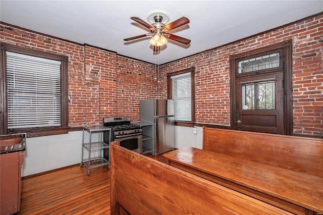 kitchen featuring ceiling fan, brick wall, appliances with stainless steel finishes, and light hardwood / wood-style flooring