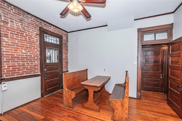 dining area featuring hardwood / wood-style floors, ceiling fan, crown molding, and brick wall