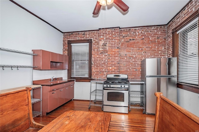 kitchen featuring hardwood / wood-style floors, stainless steel appliances, ceiling fan, and brick wall