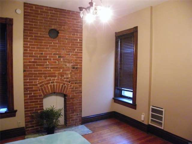 unfurnished living room featuring a notable chandelier, wood-type flooring, and heating unit