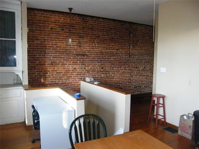 dining room featuring dark wood-type flooring and brick wall