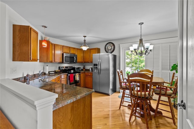 kitchen with an inviting chandelier, kitchen peninsula, decorative light fixtures, appliances with stainless steel finishes, and light wood-type flooring