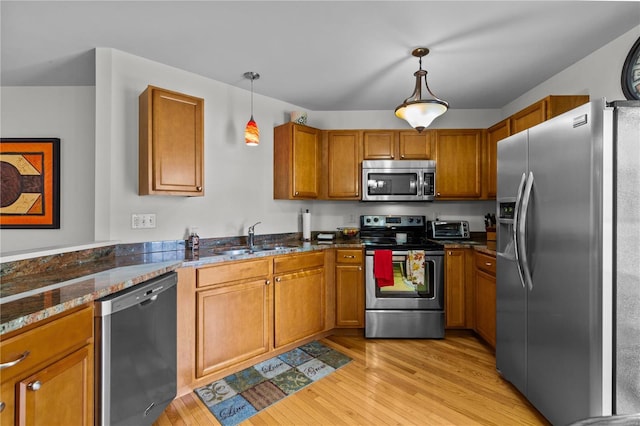 kitchen featuring pendant lighting, dark stone counters, sink, light hardwood / wood-style flooring, and appliances with stainless steel finishes