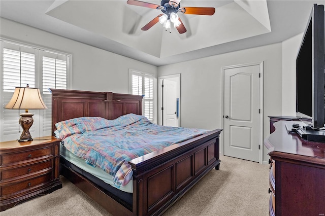 carpeted bedroom with ceiling fan and a tray ceiling