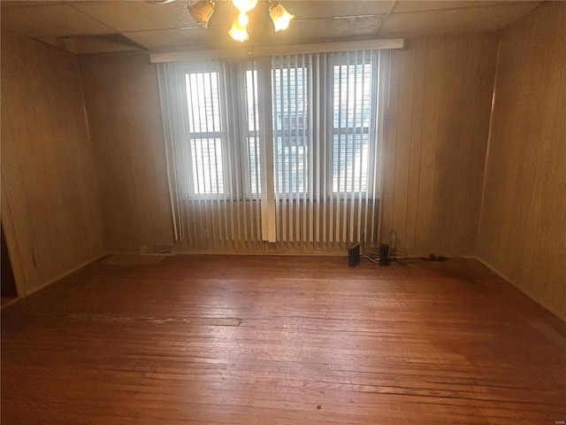 empty room with a drop ceiling, hardwood / wood-style flooring, and wood walls