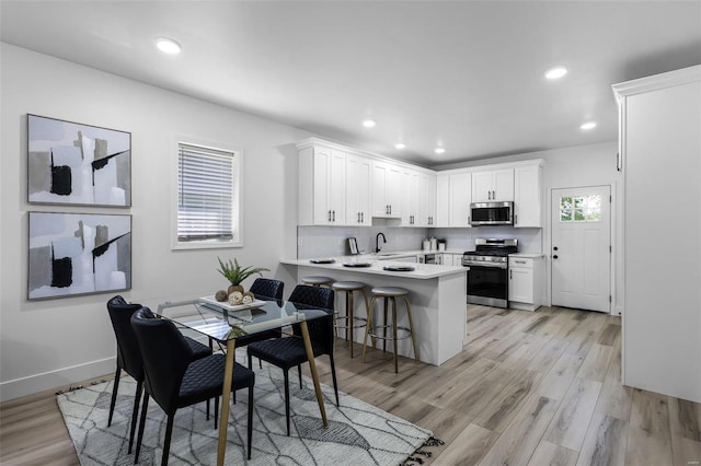 kitchen featuring stainless steel appliances, kitchen peninsula, white cabinets, and light wood-type flooring