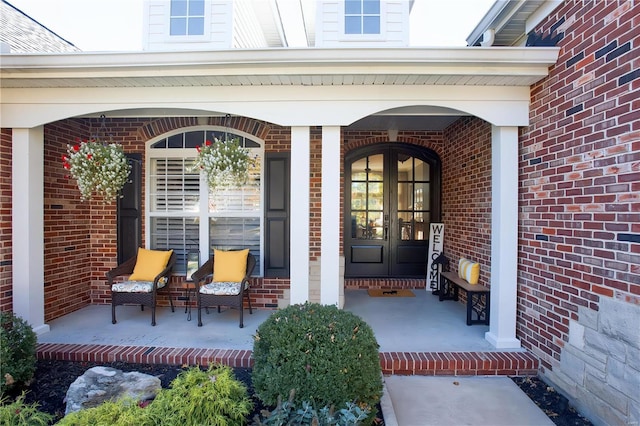 view of exterior entry featuring french doors, a porch, and brick siding