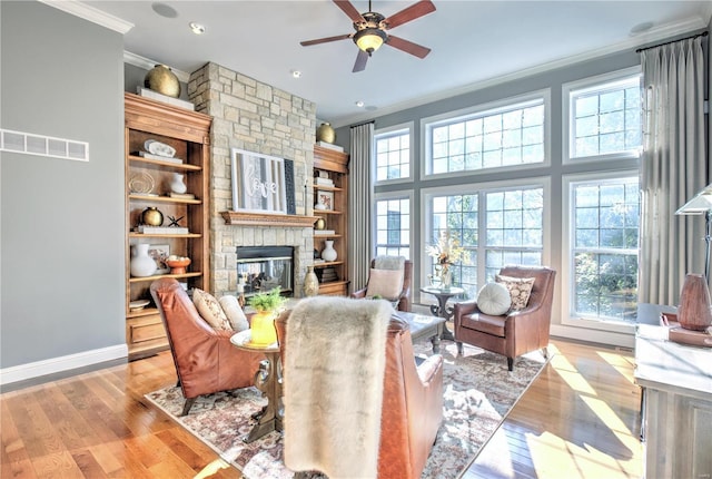 living room with ornamental molding, light wood-type flooring, visible vents, and a stone fireplace