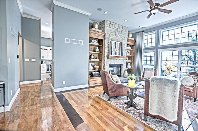 living area with a fireplace, visible vents, ornamental molding, wood finished floors, and baseboards