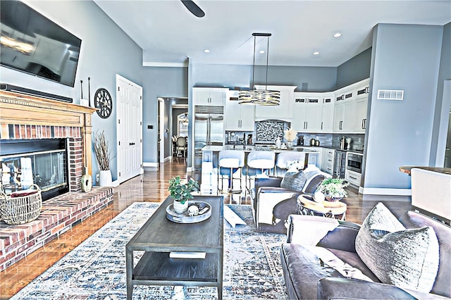 living room with recessed lighting, dark wood-type flooring, visible vents, baseboards, and a brick fireplace