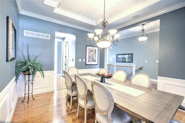 dining space with a wainscoted wall, light wood finished floors, a raised ceiling, visible vents, and ornamental molding