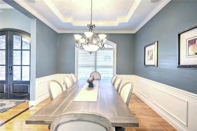 dining area with french doors, a raised ceiling, light wood-style flooring, and an inviting chandelier