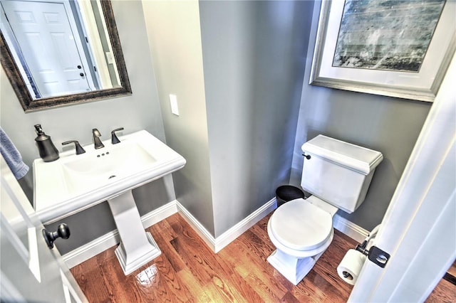 half bath with toilet, baseboards, and wood finished floors