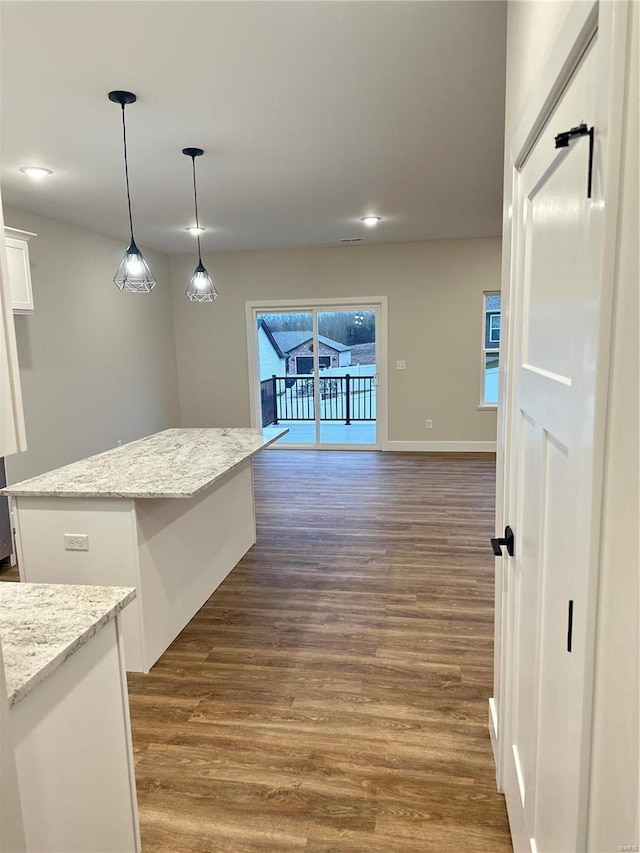 kitchen featuring pendant lighting, a center island, white cabinets, light stone countertops, and dark hardwood / wood-style flooring