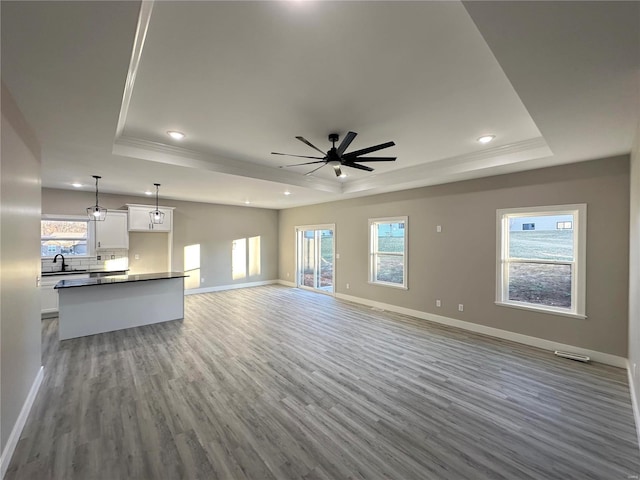 unfurnished living room with ceiling fan, a raised ceiling, and light wood-type flooring