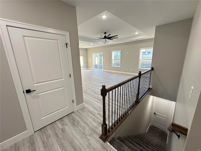 stairway with a raised ceiling, wood-type flooring, and ceiling fan