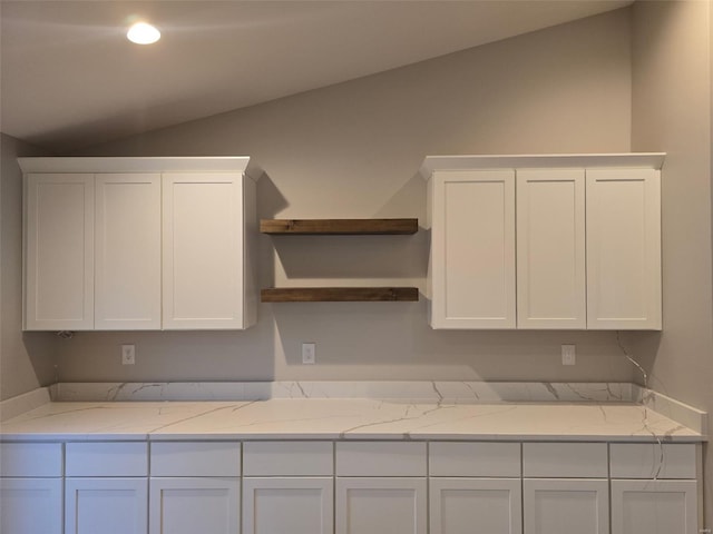 kitchen with lofted ceiling, light stone counters, and white cabinets