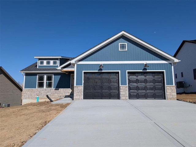 view of front of property with stone siding, cooling unit, concrete driveway, and a garage