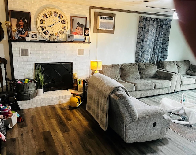 living room with hardwood / wood-style floors, an AC wall unit, and a brick fireplace