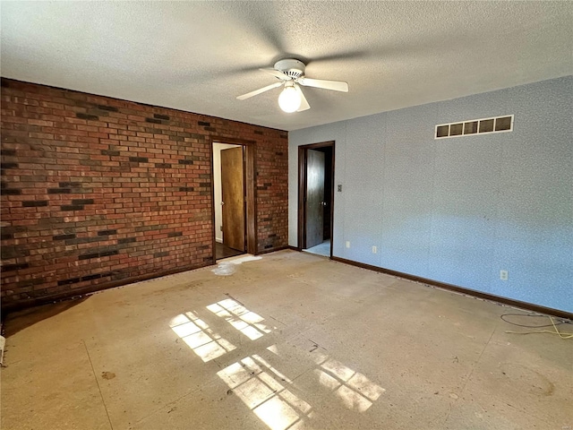 empty room featuring ceiling fan, brick wall, and a textured ceiling