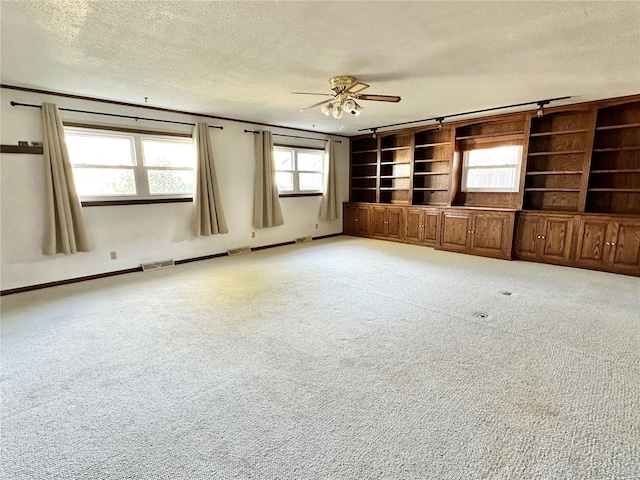 spare room with built in shelves, ceiling fan, a textured ceiling, and light carpet