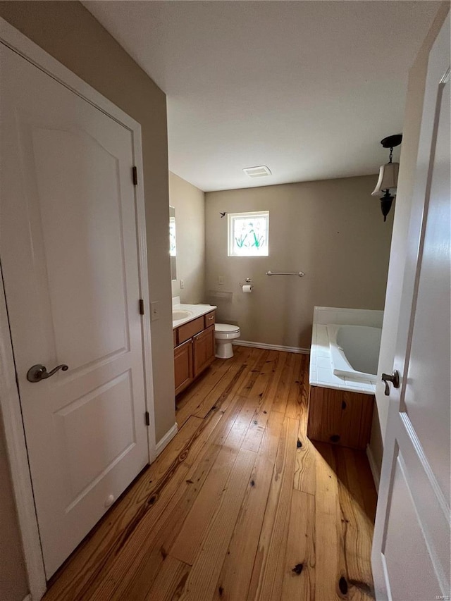 bathroom with a bath, vanity, hardwood / wood-style floors, and toilet