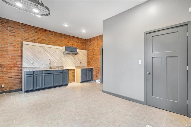 kitchen with ventilation hood, brick wall, and blue cabinetry