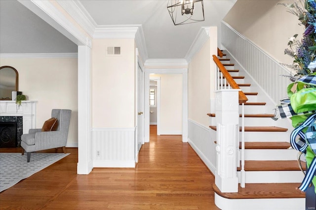 stairway featuring visible vents, a wainscoted wall, wood finished floors, a fireplace, and crown molding