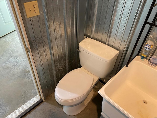 bathroom with wooden walls, toilet, sink, and concrete floors