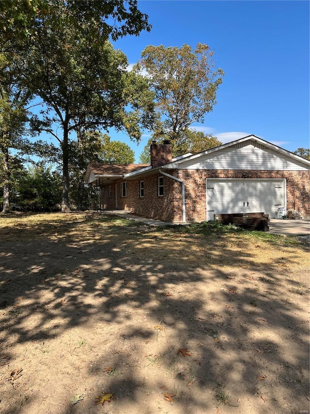 view of property exterior featuring brick siding, a garage, dirt driveway, and a chimney