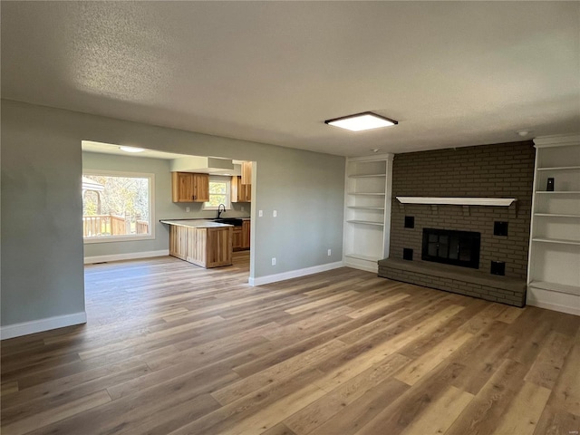 unfurnished living room featuring a textured ceiling, sink, hardwood / wood-style floors, and a brick fireplace