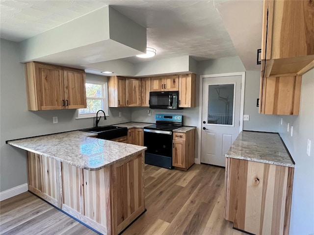 kitchen featuring a peninsula, black microwave, range with electric stovetop, a sink, and light wood finished floors
