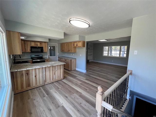 kitchen featuring a peninsula, black microwave, stainless steel electric stove, a sink, and light wood finished floors