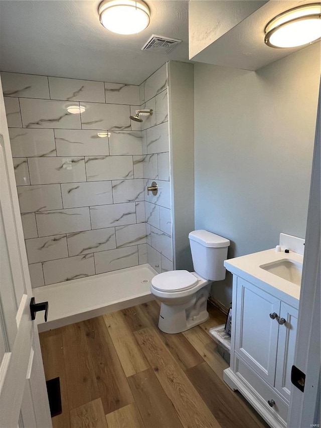 full bath featuring visible vents, a tile shower, wood finished floors, vanity, and toilet